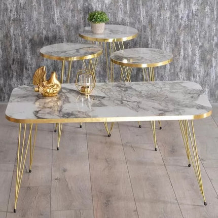 Set of marble tables with gold frames on a wooden floor against a gray stone wall.
