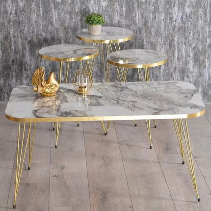Set of marble tables with gold frames on a wooden floor against a gray stone wall.