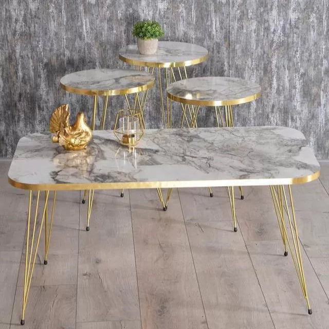 Set of marble tables with gold frames on a wooden floor against a gray stone wall.